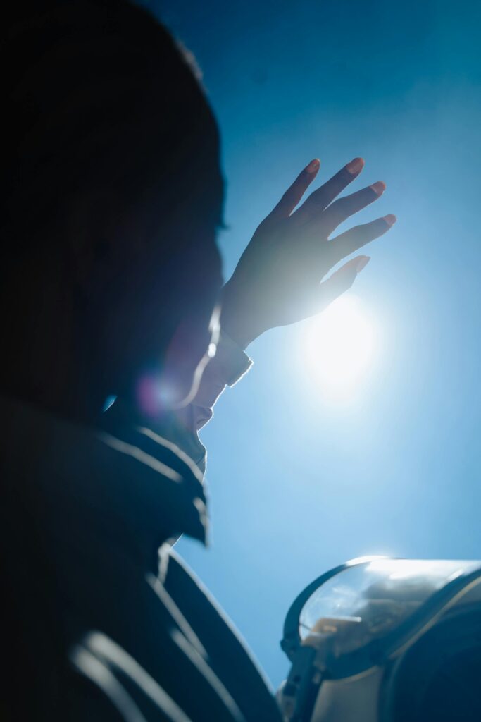 Silhouette of a spacewoman shielding her eyes from bright sunlight with a raised hand.